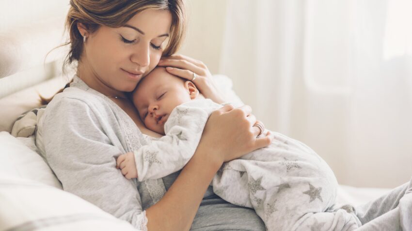 Mama troskliwie przytula noworodka, okazując mu czułość i opiekę. Stwardnienie guzowate to rzadkie schorzenie genetyczne, które może ujawniać się już we wczesnym dzieciństwie, wpływając na rozwój dziecka.