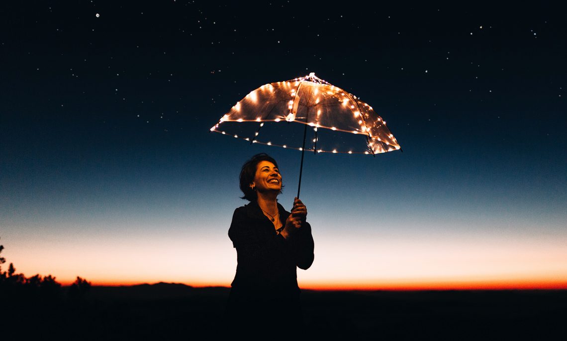Tekst o cechach wyróżniających szczęśliwych ludzi. Na zdjęciu: Kobieta trzymająca zapaloną parasolkę - HelloZdrowie
