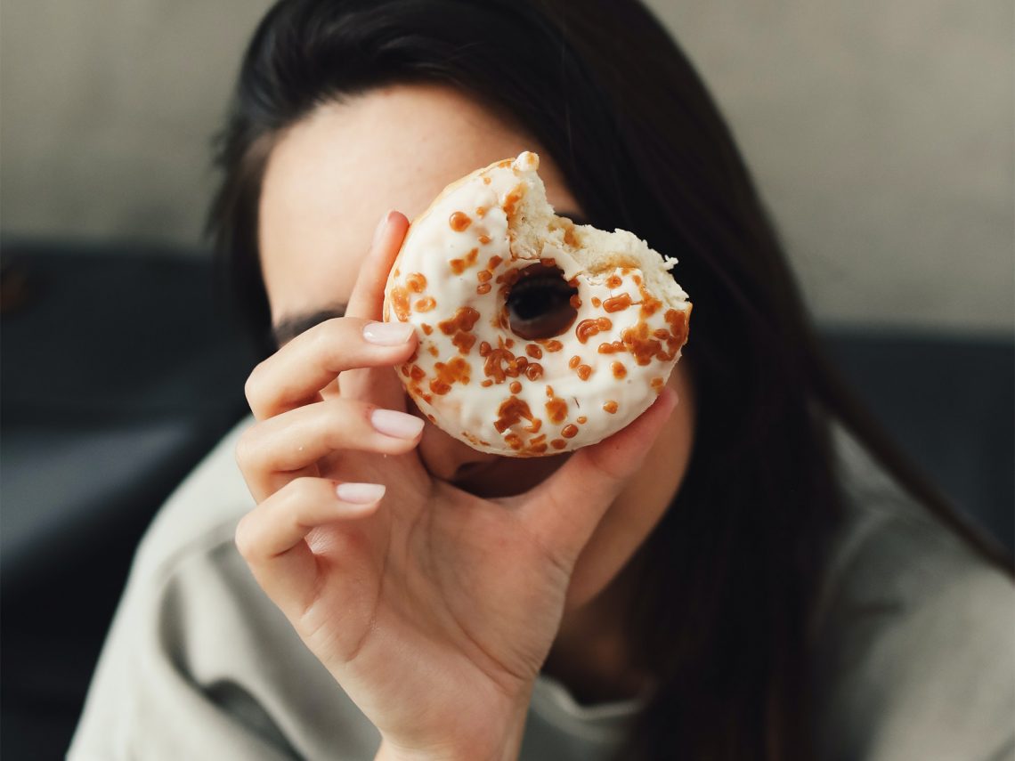 Tekst o produktach szkodliwych dla zdrowia serca. Na zdjęciu: Kobieta trzymająca donut - HelloZdrowie