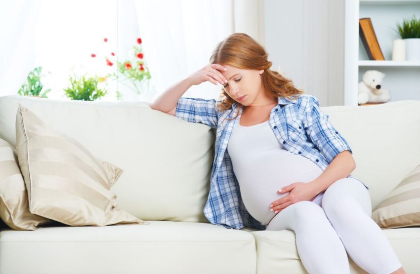 Kobieta w ciąży siedząca na kanapie i stresująca się
