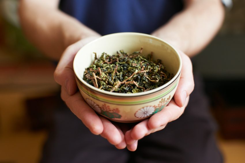 Tekst o wpływie zielonej herbaty na metabolizm. Na zdjęciu: Osoba trzymająca miseczkę z zielonymi liśćmi - HelloZdrowie