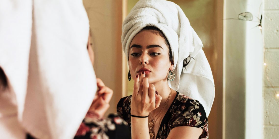 Tekst o wpływie makijażu na trądzik i skórę. Na zdjęciu: Kobieta nakładająca pomadkę do ust - HelloZdrowie