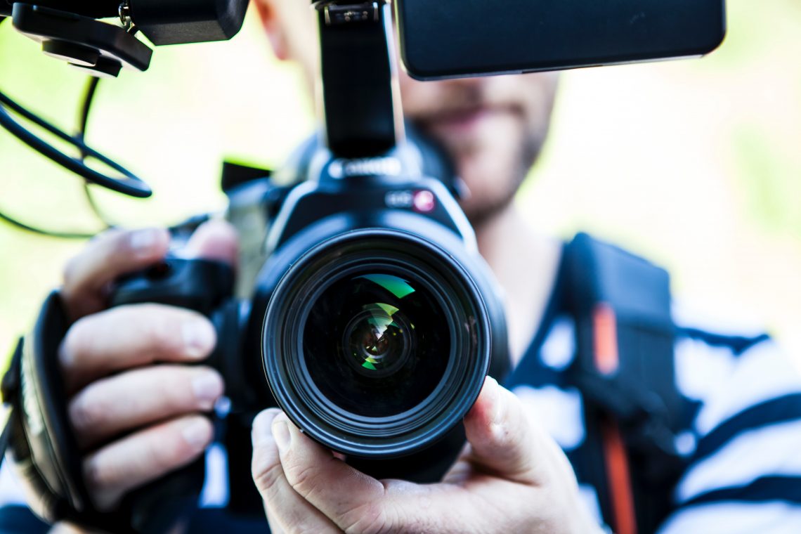 Tekst o pracy jako młodszy(a) realizator(ka) vlogów. Na zdjęciu: Mężczyzna trzymający aparat fotograficzny - HelloZdrowie