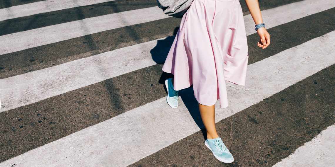 Tekst o aktywności bez potrzeb siłowni. Na zdjęciu: Osoba idąca w różowej spódnicy i niebieskich butach przechodząca przez ulicę - HelloZdrowie