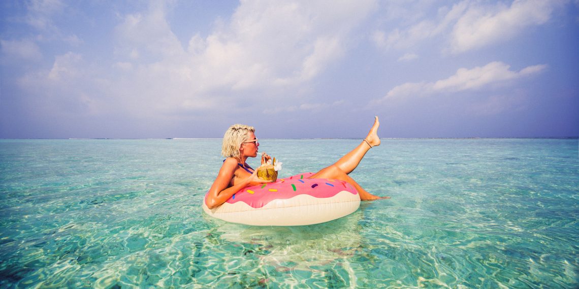 Po ilu wolnych dniach zaczynamy odpoczywać? Na zdjęciu kobieta na dmuchanym kole kąpię się w morzu i pije drinka.
