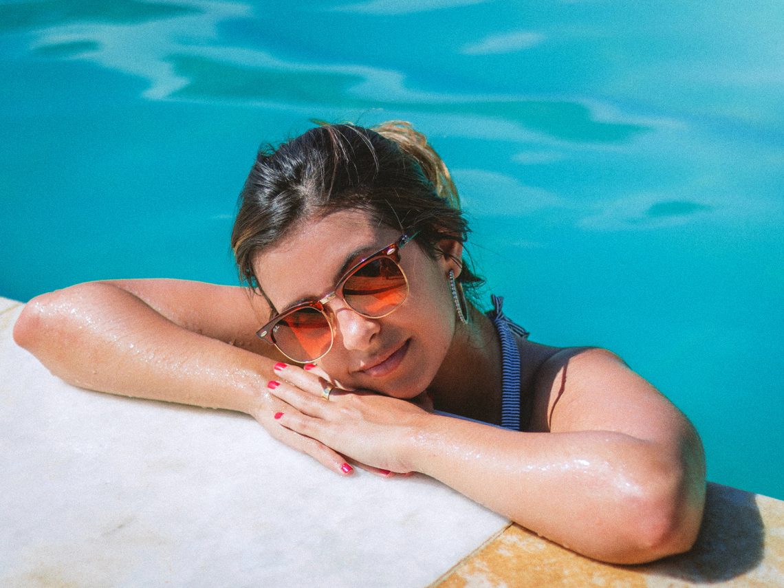 Tekst o zasadach zapobiegania infekcjom intymnym na wakacjach. Na zdjęciu: Kobieta w kostiumie kąpielowym opierająca się na krawędzi basenu - HelloZdrowie