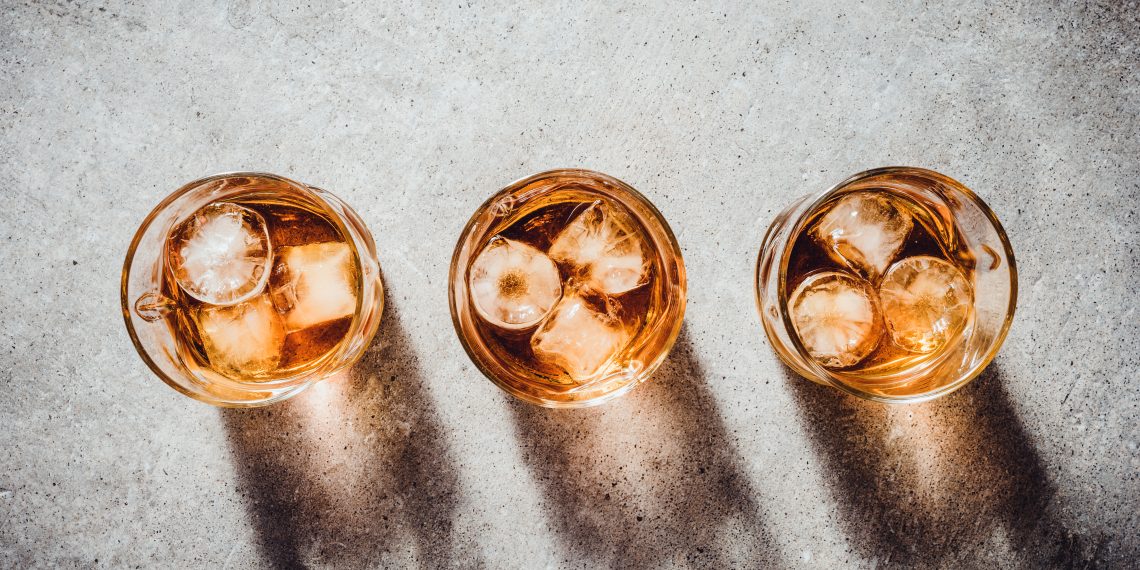 Tekst o zdrowotnych zaletach i smakowaniu whisky. Na zdjęciu: Grupa szklanek z lodem i bursztynowym płynem - HelloZdrowie