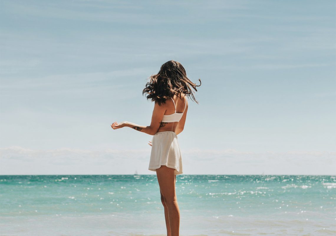 Tekst o suplementacji witaminy D3 w okresie letnim. Na zdjęciu: Kobieta stojąca na plaży - HelloZdrowie