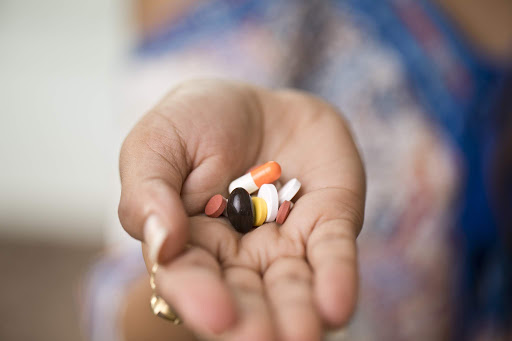 Tekst o znaczeniu, niedoborach i suplementacji witaminy B12. Na zdjęciu: Ręka trzymająca garstkę tabletek - HelloZdrowie