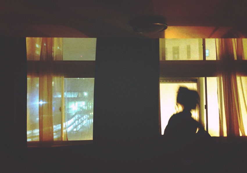 Czym są urojenia i jakie ich rodzaje wyróżnia się w psychologii, na zdjęciu kobieta w ciemnym pokoju na tle okna- Hello Zdrowie
