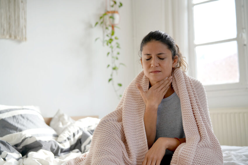 na zdjęciu: kobieta siedzi na łóżku, tekst o: bólu migdałków u dzieci i dorosłych /fot. Adobe Stock