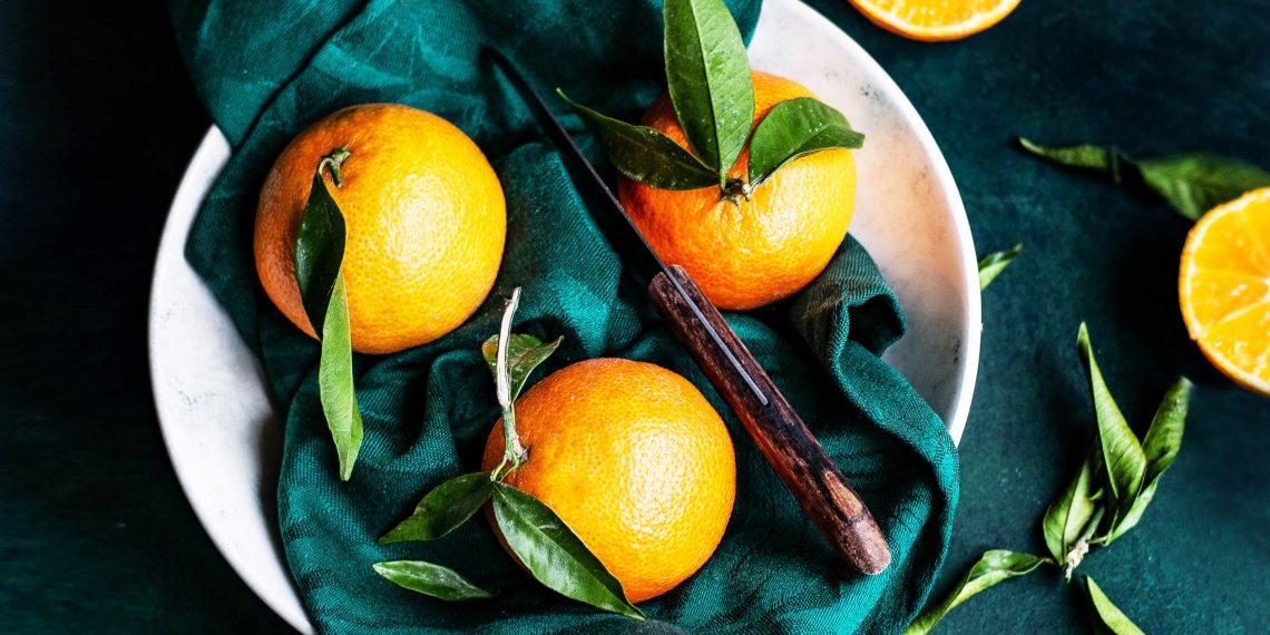 Trzy pomarańcze i nóż leżą na talerzy pokrytym ścierką