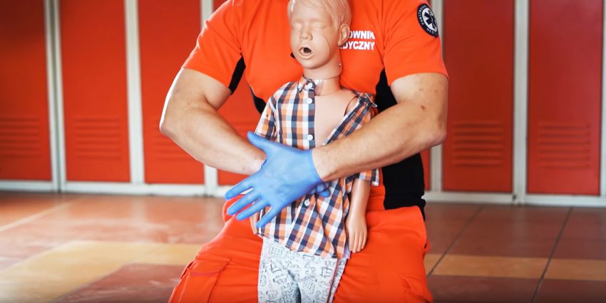 Ratownik medyczny z manekinem dziecka pokazuje jak udzielić pierwszej pomocy, kiedy dziecko się zadławi