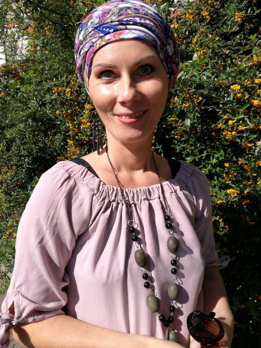 Tekst o walce z rakiem i terapii psychologicznej. Na zdjęciu: Kobieta nosząca chustkę na głowie i uśmiechającą się - HelloZdrowie