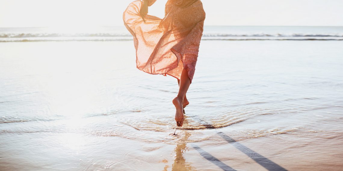 Kobieta biegnie po plaży przy linii morza. ma zwiewną sukienkę