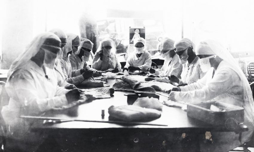 Tekst o pandemii grypy z lat 1918-1920. Na zdjęciu: Grupa ludzi w białych płaszczach i maskach siedząca przy stole - HelloZdrowie