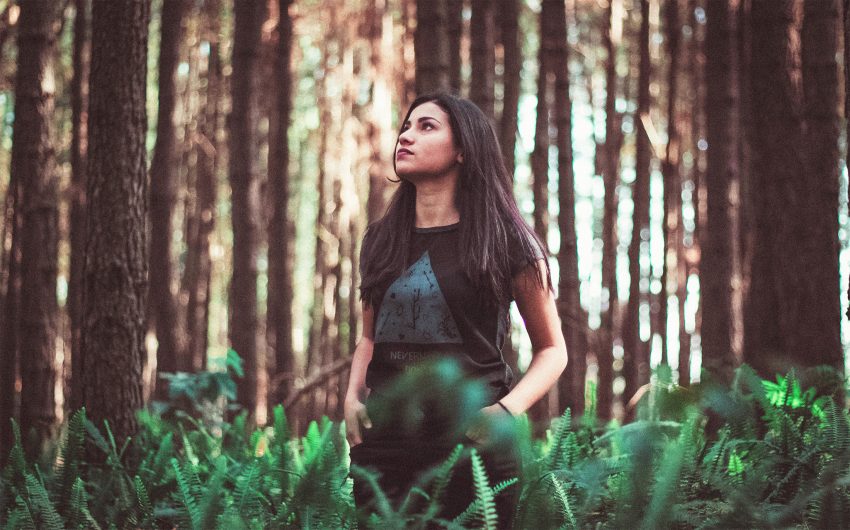 Kobieta stoi w lesie i patrzy na drzewa
