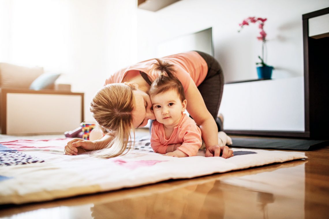 Kobieta całuje córkę w policzko, ćwicząc na podłodze