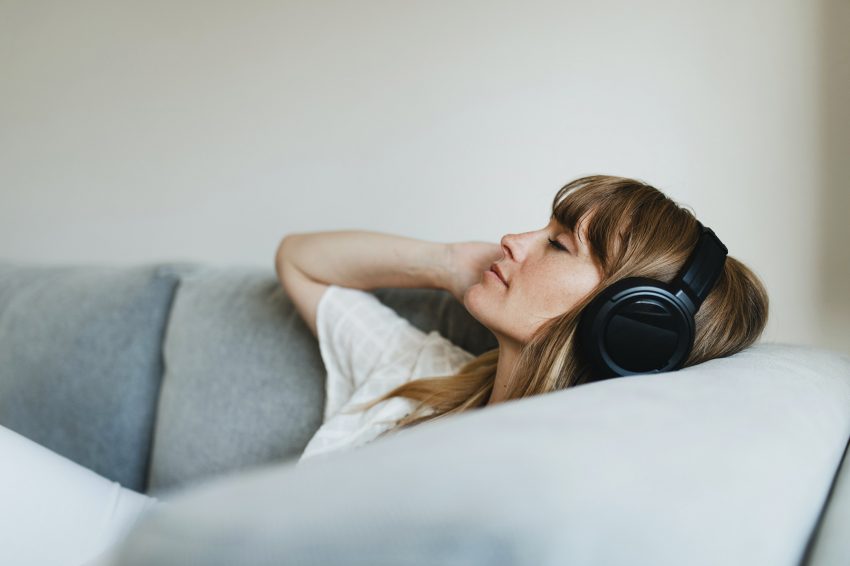 Kobieta leży na kanapie i słucha muzyki przez słuchawki