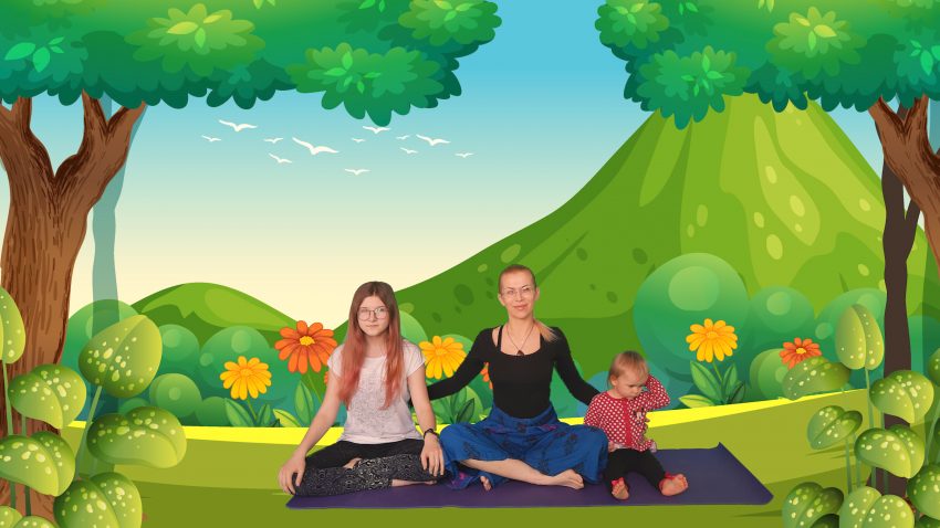 Tekst o korzyściach jogi dla dzieci według ekspertki. Na zdjęciu: Grupa ludzi siedzi na macie przed zielonym krajobrazem - HelloZdrowie