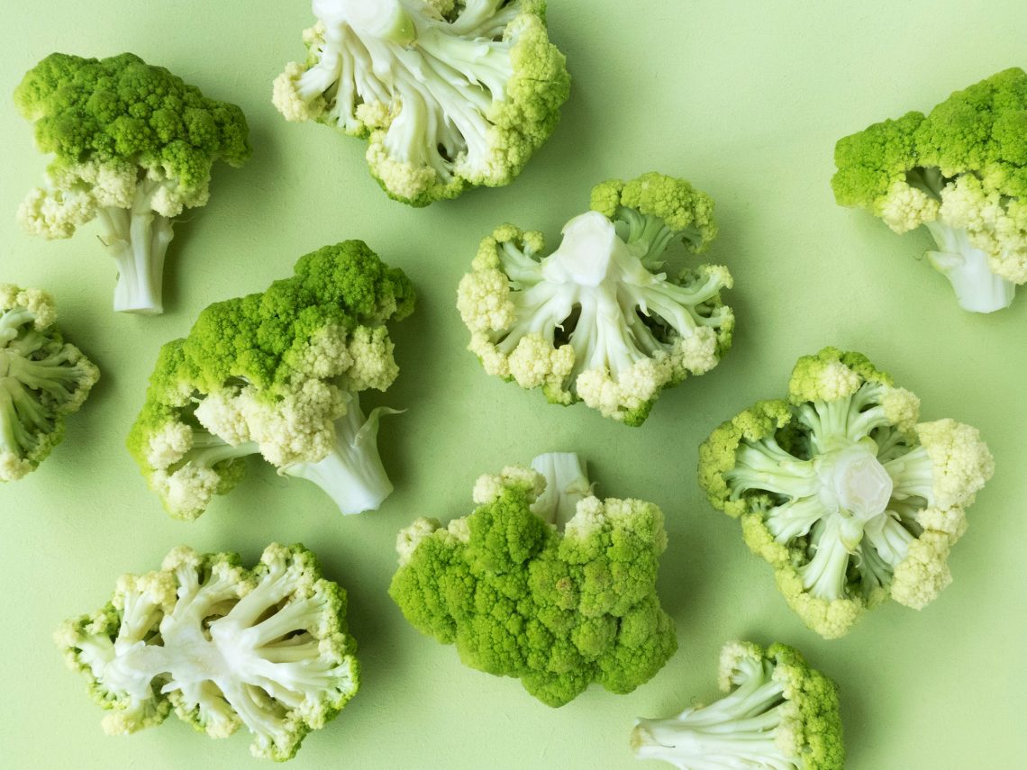 Tekst o: wartościach odżywczych mrożonych warzyw vs świeże. Na zdjęciu: Grupa brokułów na zielonej powierzchni - HelloZdrowie