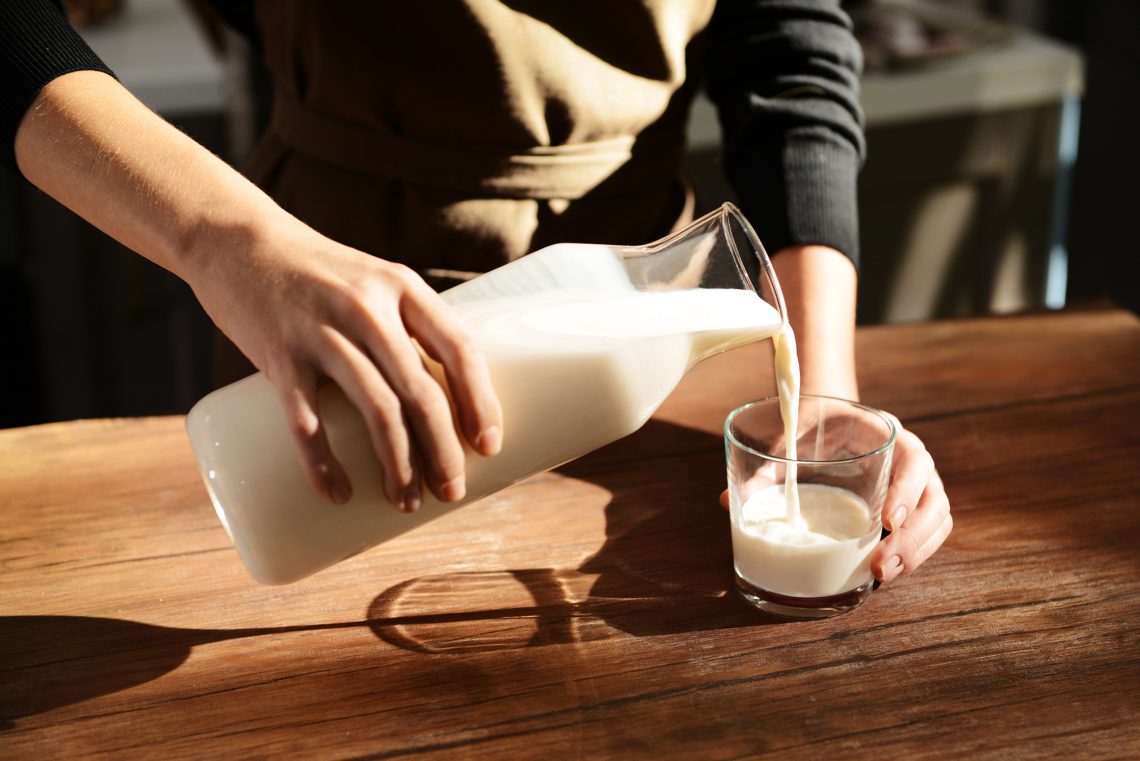 Tekst o zdrowotnych korzyściach picia mleka owsianego. Na zdjęciu: Osoba nalewająca mleko do szklanki - HelloZdrowie