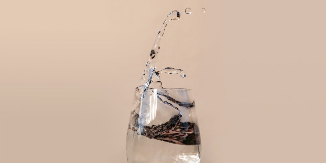 Tekst o korzyściach picia wody na czczo. Na zdjęciu: Szklanka wody z chlapaniem wody - HelloZdrowie