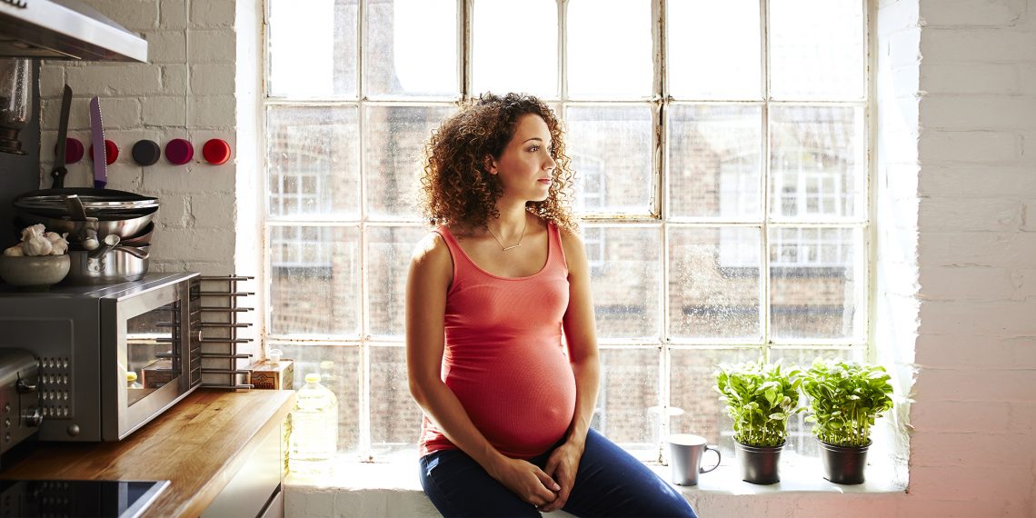 Tekst o różnych podejściach kobiet do ciąży. Na zdjęciu: Kobieta w ciąży siedzi na parapecie okna - HelloZdrowie