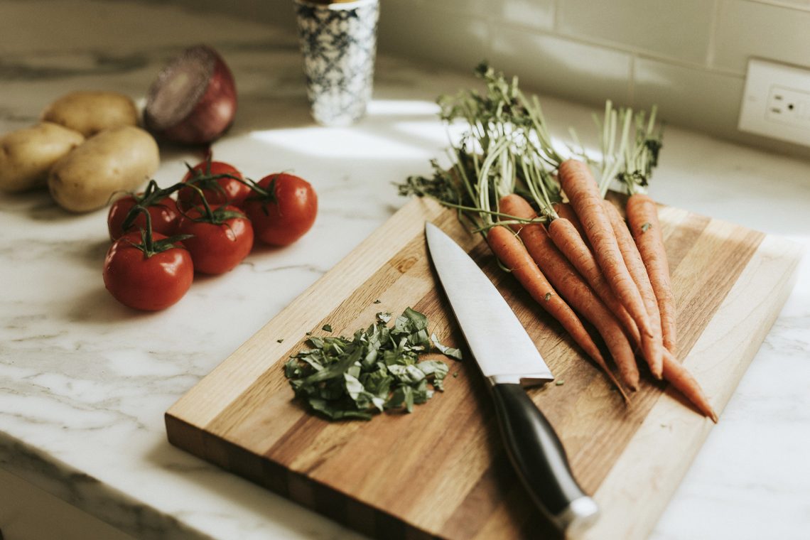 Tekst o technikach krojenia żywności jak zawodowiec. Na zdjęciu: Deska do krojenia z warzywami i nożem na niej - HelloZdrowie