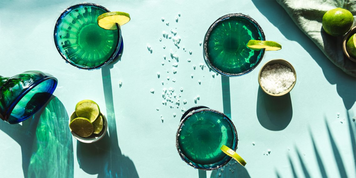Tekst o wpływie pory picia alkoholu na zdrowie. Na zdjęciu: Grupa szklanek z zielonym płynem i plasterkami limonki - HelloZdrowie
