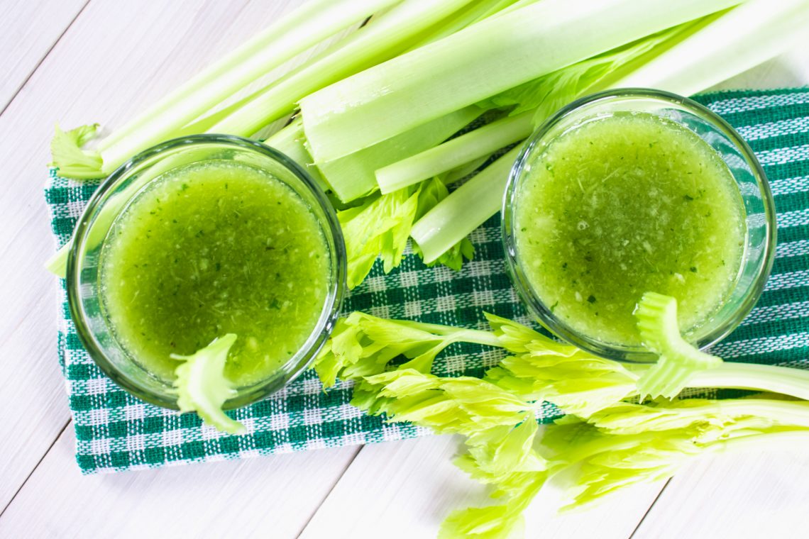 Tekst o korzyściach zdrowotnych picia soku z selera. Na zdjęciu: Dwa szklanki zielonej cieczy obok selera - HelloZdrowie