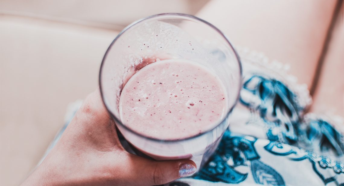 Tekst o różnicach między jogurtem greckim a zwykłym. Na zdjęciu: Ręka trzymająca szklankę milkshaku - HelloZdrowie