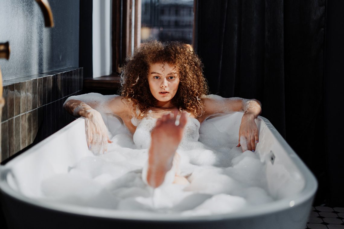 Tekst o optymalizowaniu relaksującej kąpieli dodatkami. Na zdjęciu: Kobieta w wannie z pianą - HelloZdrowie