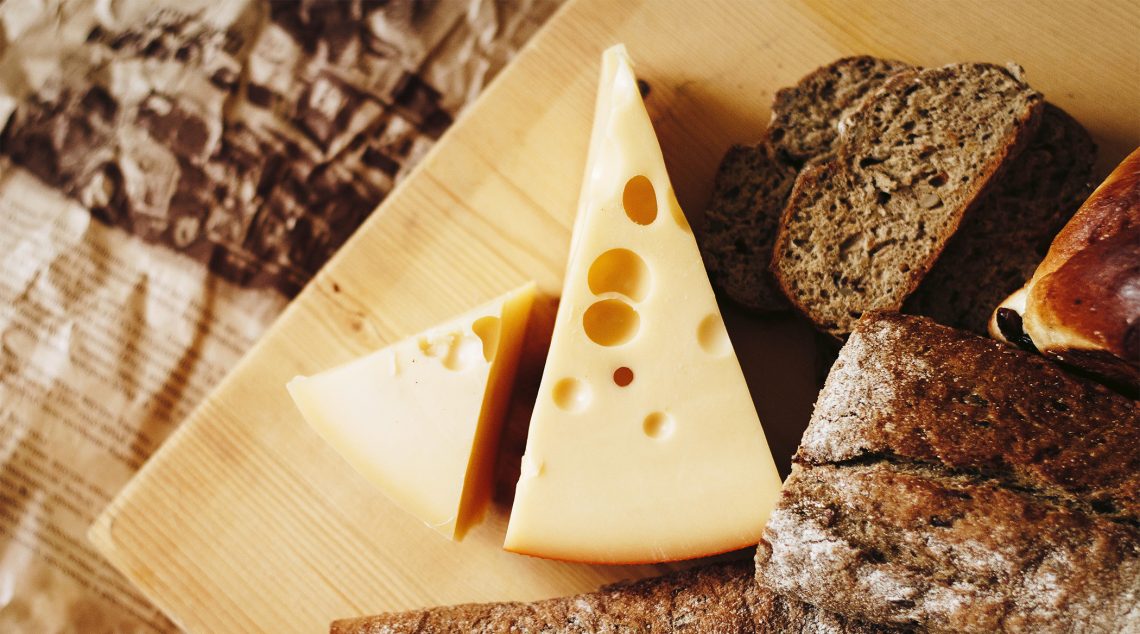Tekst o korzyściach zdrowotnych i wartościach odżywczych sera. Na zdjęciu: Ser żółty i chleb na desce do krojenia - HelloZdrowie
