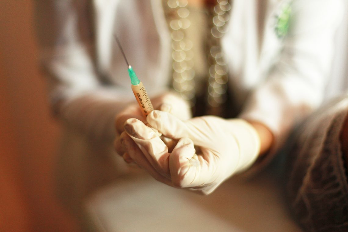 Tekst o konieczności szczepień przeciw grypie i COVID-19. Na zdjęciu: Osoba trzymająca strzykawkę - HelloZdrowie