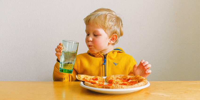 Dziecko je posiłek przy stole i pije wodę ze szklanki
