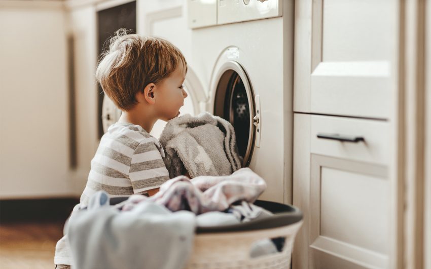 Chłopiec wkłada ciuchydo pralki