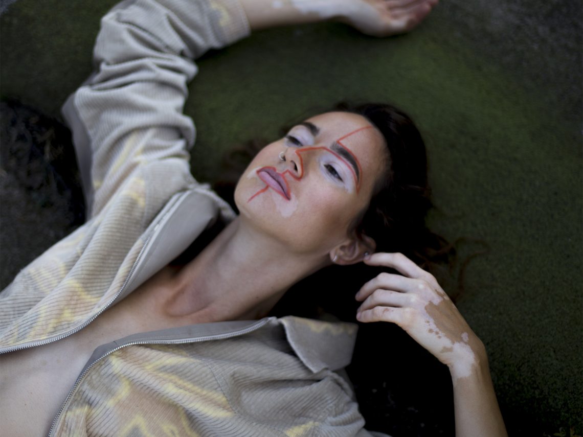 Tekst o pięknie kobiet z bielactwem przez fotografie. Na zdjęciu: Kobieta leżąca na ziemi z ręką na twarzy - HelloZdrowie