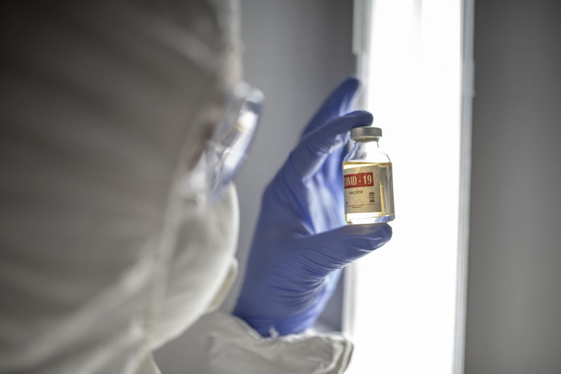 Tekst o szwajcarskiej decyzji ws. zatwierdzenia szczepionek. Na zdjęciu: Osoba w białym garniturze i okularach trzymająca małą butelkę płynu - HelloZdrowie