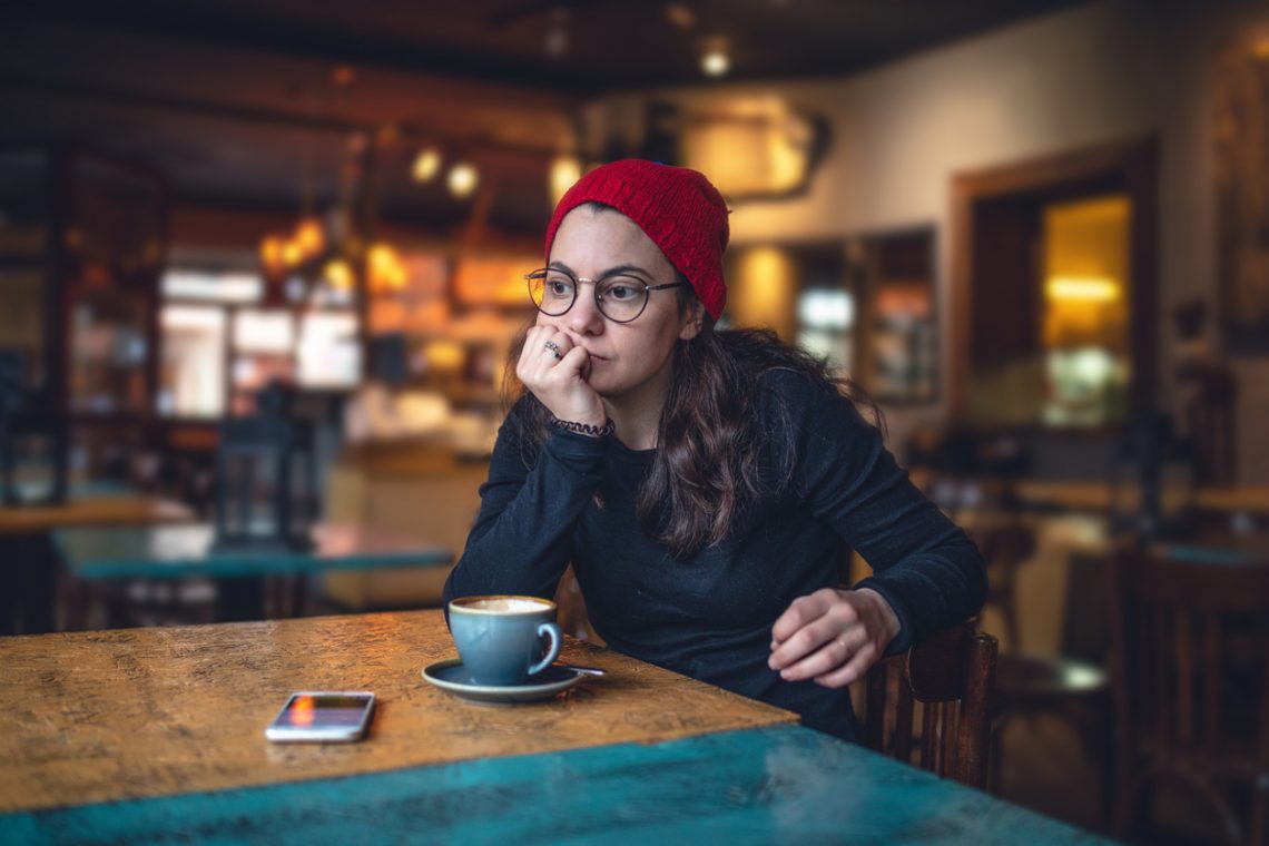 Tekst o trudnych świętach dla osób LGBTQIA+. Na zdjęciu: Kobieta siedząca przy stole z filiżanką kawy - HelloZdrowie