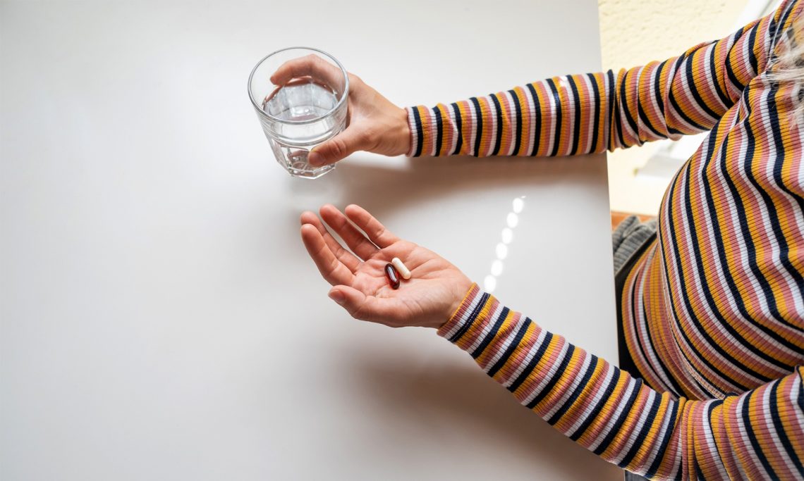 Tekst o płukaniu żołądka: procedura, wskazania, powikłania. Na zdjęciu: Osoba trzymająca pigułkę i szklankę wody - HelloZdrowie