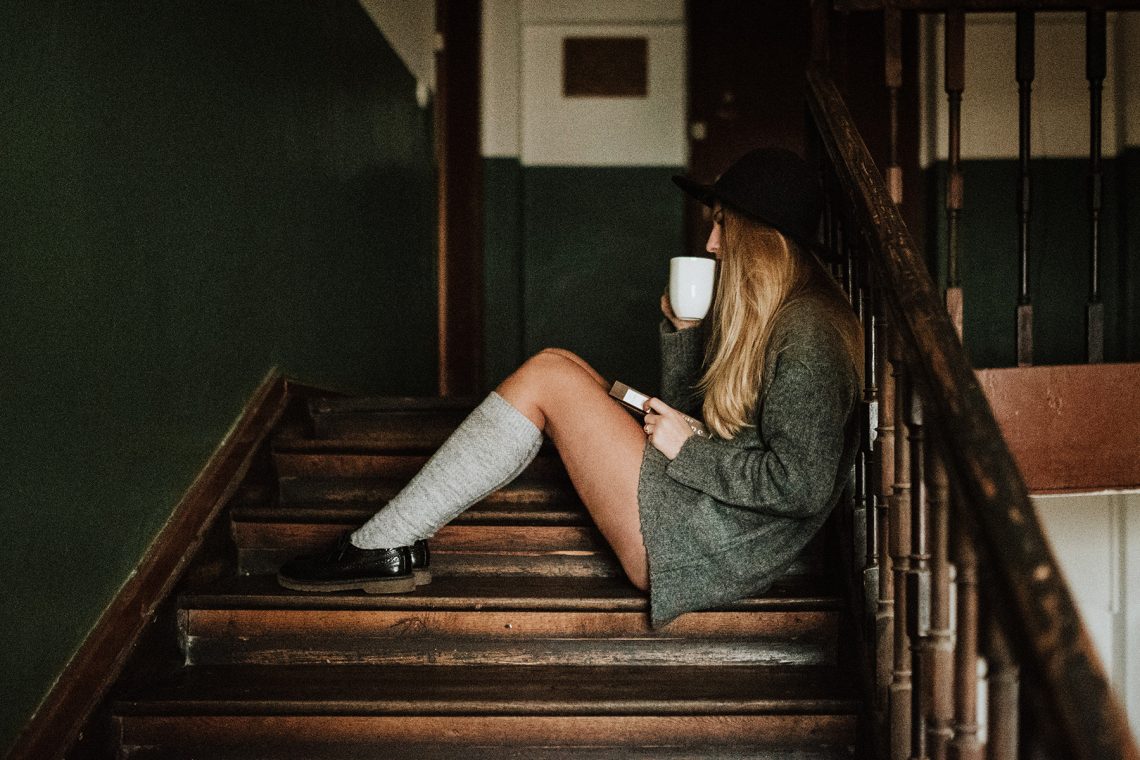 Tekst o ziołach wspomagających leczenie schorzeń nerek. Na zdjęciu: Kobieta siedząca na schodach trzymająca filiżankę i książkę - HelloZdrowie