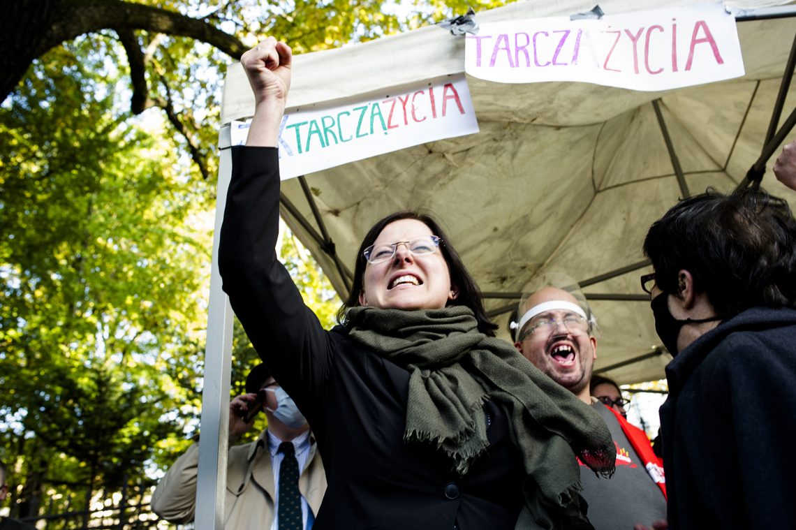 Tekst o nagrodzie za wypowiedzi sprzeczne z nauką. Na zdjęciu: Kobieta podnosi swoją pięść przed grupą ludzi - HelloZdrowie