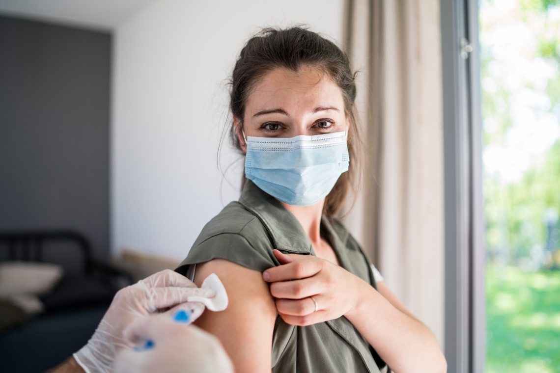 Tekst o historii lęku przed szczepieniami. Na zdjęciu: Kobieta w masce na twarz i rękawiczkach dostaje zastrzyk - HelloZdrowie