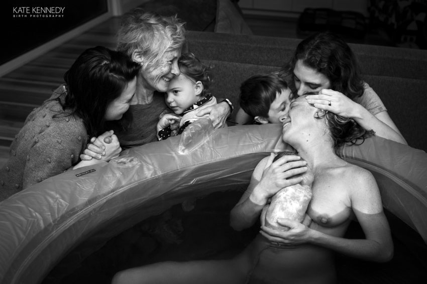 Kobieta rodzi w basenie w domu w otoczeniu rodziny