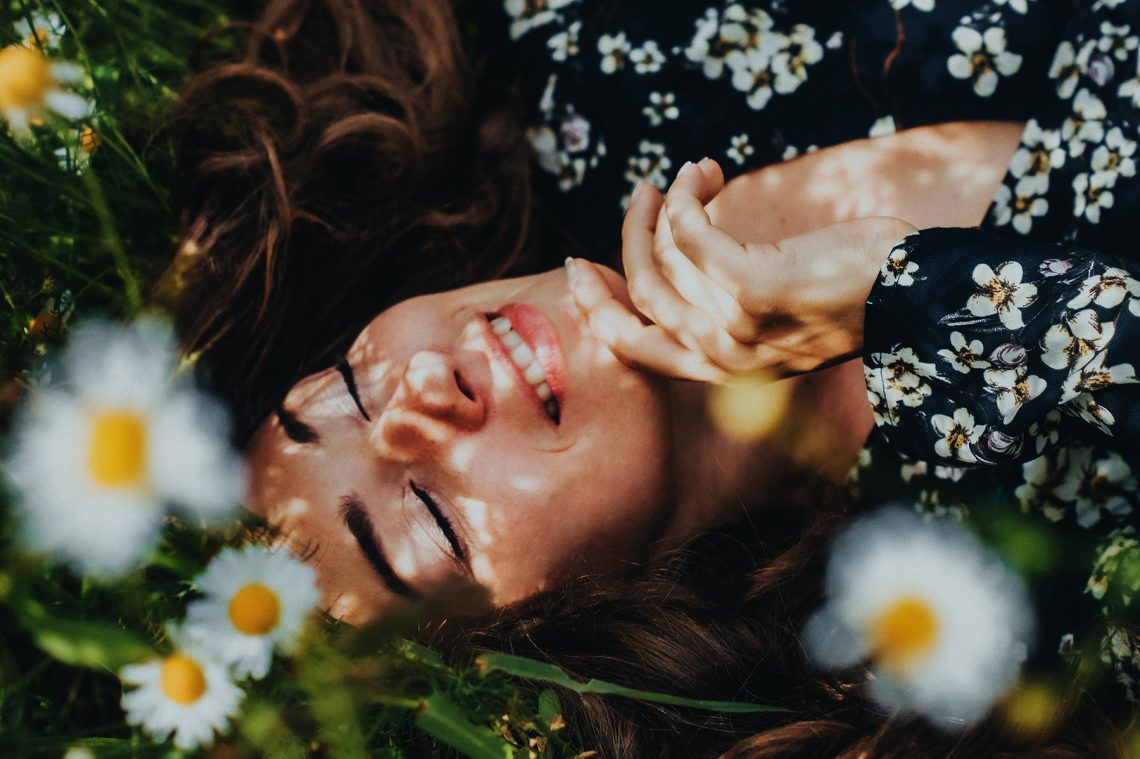 Tekst o nakładkach na zęby i ich kosztach. Na zdjęciu: Kobieta leżąca na polu kwiatów - HelloZdrowie