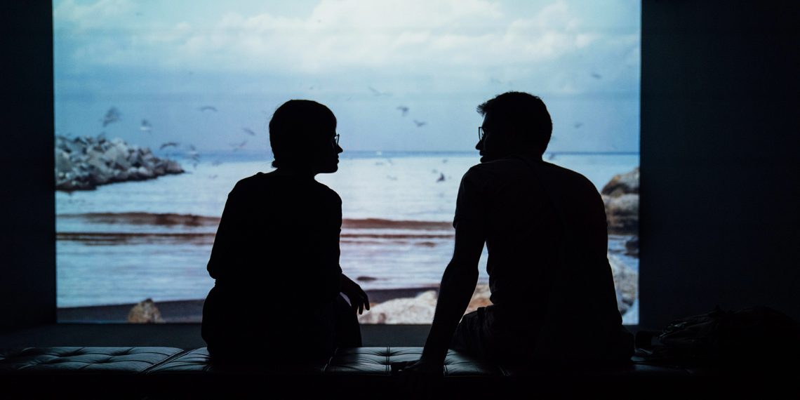 Tekst o nowym płatnym urlopie żałobnym w Nowej Zelandii. Na zdjęciu: Sylwetka dwóch osób siedzących na kanapie i patrzących na plażę - HelloZdrowie
