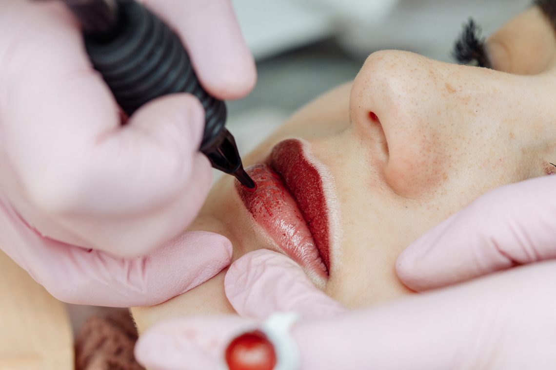 Tekst o makijażu permanentnym ust i jego bezpieczeństwie. Na zdjęciu: Osoba robiąca tatuaż na ustach - HelloZdrowie