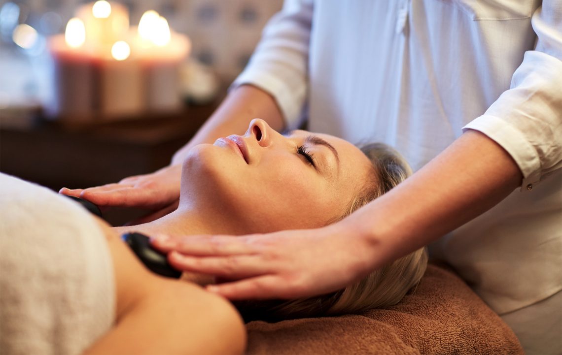Tekst o masażu gorącymi kamieniami, jego zaletach i przeciwwskazaniach. Na zdjęciu: Kobieta otrzymująca masaż - HelloZdrowie