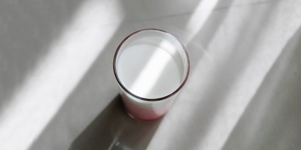 Tekst o diecie i zaleceniach przy refluksie żołądkowym. Na zdjęciu: Szklanka mleka na białej powierzchni - HelloZdrowie